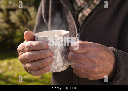 Réchauffer le froid les mains avec une tasse de thé chaud après le jardinage sur journée ensoleillée d'automne froid Banque D'Images