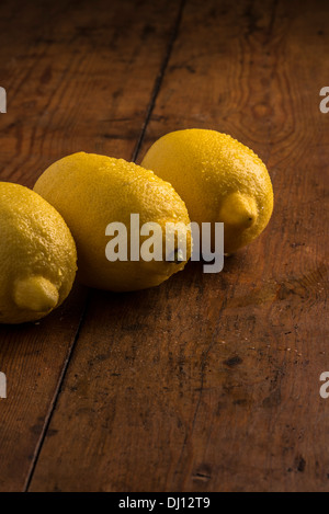 Trois citrons frais alignés dans une nature morte avec un éclairage chaleureux sur la vieille table en bois Banque D'Images
