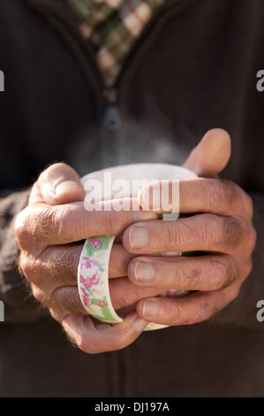 Réchauffer le froid les mains avec une tasse de thé chaud après le jardinage sur journée ensoleillée d'automne froid Banque D'Images