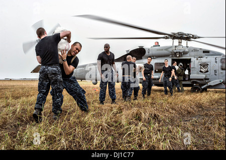 Les marins de l'US Navy forment une ligne pour charger des fournitures de secours sur un MH-60R Seahawk pour distribution aux villages éloignés dans le sillage de super typhon Haiyan, le 17 novembre 2013 à Tacloban, Philippines. Banque D'Images