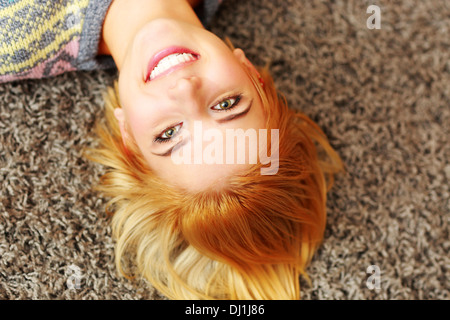 Closeup portrait of a smiling young woman lying on the carpet at home Banque D'Images