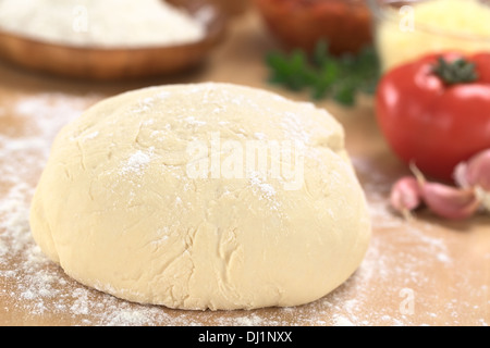 Pâte à pizza maison sur planche en bois farinée avec pizza ingrédients (farine, tomate, fromage râpé et d'herbes) dans l'arrière Banque D'Images