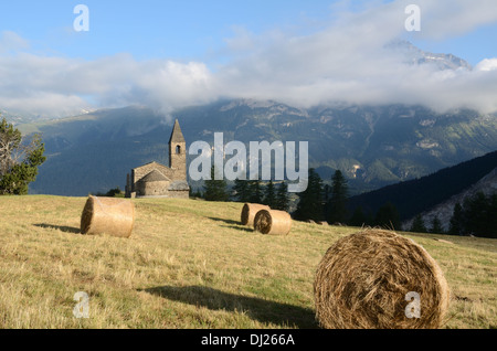 Vue Panoramique Sur L'Église Ou L'Église St-Pierre Extravache Et Les Balles De Foin Sur Le Pâturage Alpin Bramans Haute Maurienne Savoie Alpes Françaises France Banque D'Images