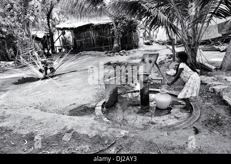 Indian girl le remplissage d'eau en plastique de pot un village rural pompe à main. L'Andhra Pradesh, Inde. Noir et blanc. Banque D'Images