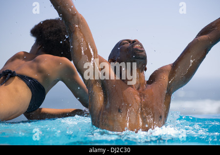 South African Male sauter de haut de exubérantes d'une piscine à débordement donnant sur l'océan tandis que sa femme les canards grand bruit. Banque D'Images