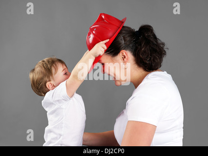 Mère et enfant jouant, petite blonde boy ou enfant en mettant un chapeau de pompier en plastique rouge sur la maman Banque D'Images