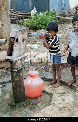 Jeune Indien le remplissage d'eau en plastique de pot un village rural pompe à main. L'Andhra Pradesh, Inde Banque D'Images