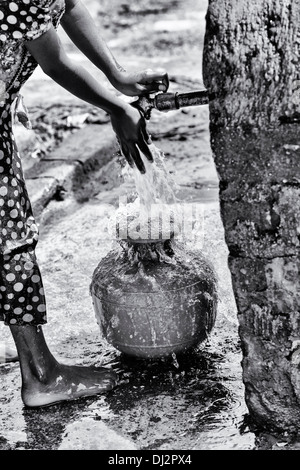 Indian girl remplissage d'un pot en plastique avec de l'eau d'un tube de mesure dans un village de l'Inde rurale. L'Andhra Pradesh, Inde. Noir et blanc. Banque D'Images