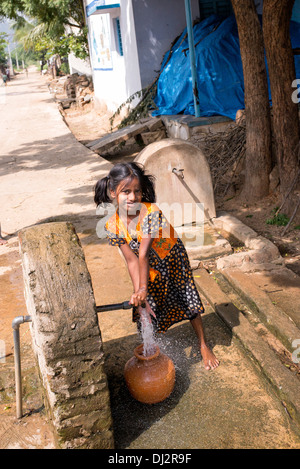 Indian girl remplissage d'un pot en plastique avec de l'eau d'un tube de mesure dans un village de l'Inde rurale. L'Andhra Pradesh, Inde Banque D'Images