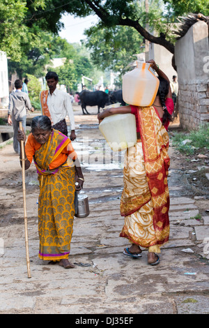 Femme indienne pots d'eau en plastique d'un tube de mesure dans une rue village. L'Andhra Pradesh, Inde Banque D'Images