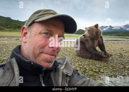 USA, Alaska, Katmai National Park, l'auto-portrait du photographe Paul Souders assis près de l'ours brun (Ursus arctos) Banque D'Images