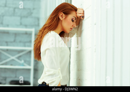 Fatigué young businesswoman leaing au wall in office Banque D'Images