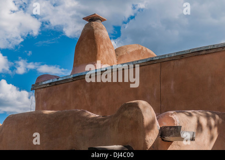 Un mur d'adobe traditionnelles avec canale pour vidanger la pluie et cheminée adobe contre ciel bleu à Santa Fe, Nouveau Mexique, USA. Banque D'Images
