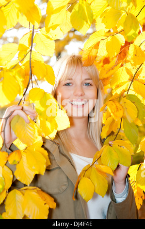 Jeune femme regarde à travers les feuilles d'automne Banque D'Images