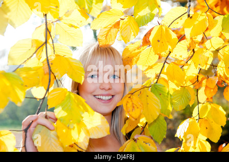 Jeune femme regarde à travers les feuilles d'automne Banque D'Images