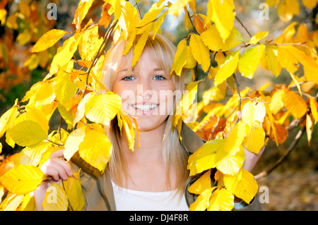 Jeune femme regarde à travers les feuilles d'automne Banque D'Images