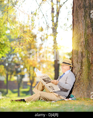 Représentant Senior assis sur une herbe de lire le journal dans un parc en automne Banque D'Images