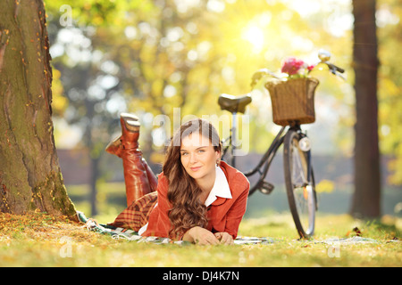 Jeune femme allongée sur l'herbe avec un vélo dans un parc sur une journée ensoleillée Banque D'Images