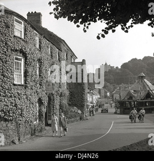 1950s, photo historique de cette époque, en regardant la rue haute de Dunster, un village datant de l'époque médiévale avec un ancien château, prieuré, dovecote, marché de fils, auberges et tearoms dans Somerset, dans le sud-ouest de l'Angleterre, Royaume-Uni. Le château de Dunster est visible au loin. Banque D'Images