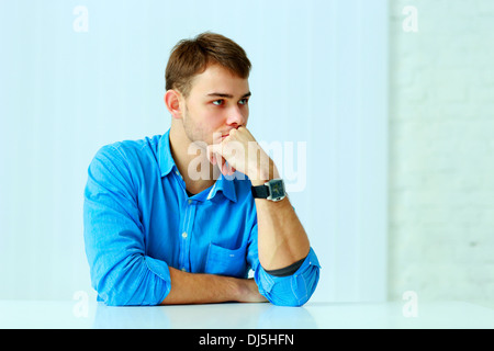 Jeune homme pensif assis à la table à l'office de tourisme Banque D'Images