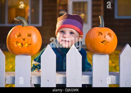 La fille de pics entre Jack-O-Lantern Visages coincé en haut de la maison, les planches en arrière-plan, au crépuscule, en Alaska. Banque D'Images