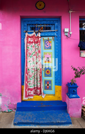 Porte avant en bois décoratif sur un bleu et rose peint maison dans un village de l'Inde rurale. L'Andhra Pradesh, Inde Banque D'Images