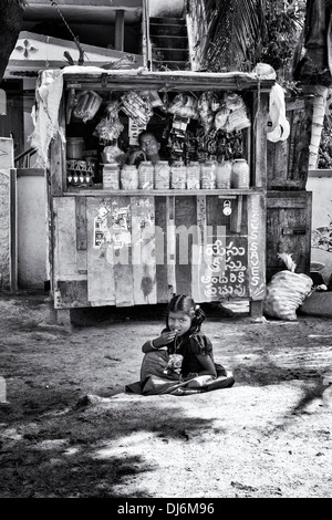 Indian girl eating collations était assis en face d'un magasin de village. L'Andhra Pradesh, Inde. Le noir et blanc Banque D'Images