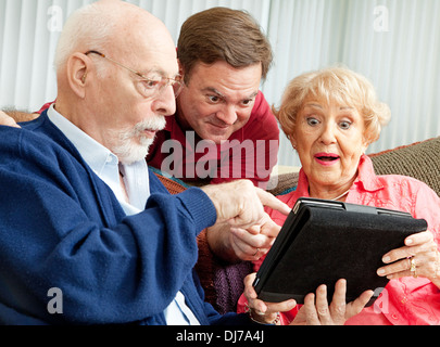 Fils adultes bénéficie d'montrant ses parents comment utiliser la nouvelle tablette PC il leur a donné comme un cadeau. Banque D'Images