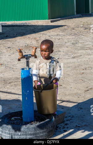 L'Afrique du Sud, Cape Town, township de Khayelitsha. Petit garçon avec godet étudiant la communauté d'un robinet d'eau. Banque D'Images