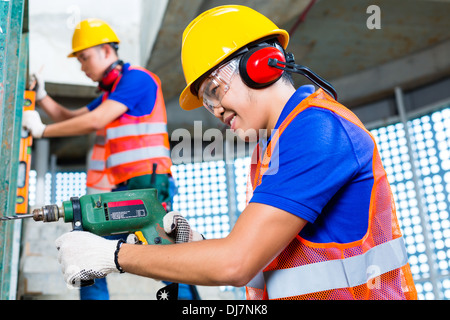 Builder indonésien asiatique ou artisan avec une machine de forage ou d'exercice, niveau à bulle, la protection des oreilles, des gants et un casque de protection ou helm Banque D'Images