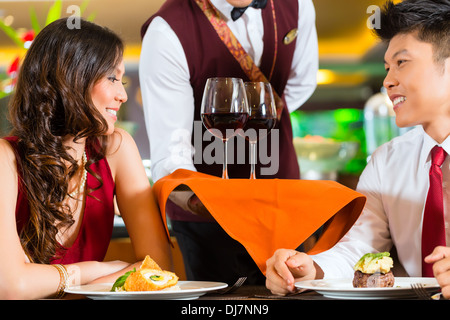 Chinois asiatique garçon ou intendant au service de l'homme et de femme ou couple dans des verres de vin rouge sur un bac dans fantaisie restaurant ou hôtel Banque D'Images