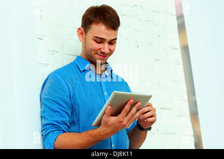 Young happy businessman standing with tablet computer près du mur Banque D'Images