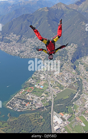 Cette femme parachutiste tombe gratuitement dans une position tête vers le bas sur une ville à côté d'une vue magnifique sur la montagne et la superficie du lac. Banque D'Images