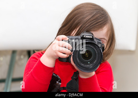 Jeune fille avec le syndrome de Down posant avec un appareil photo Canon 20D sur un fond blanc. Banque D'Images