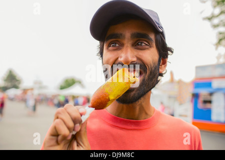 Asian man eating corn dog outdoors Banque D'Images