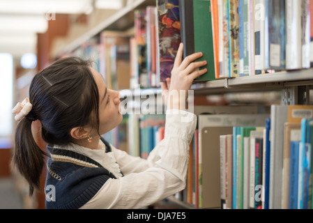 Jeune étudiante mettant un livre vert sur une étagère dans la bibliothèque Banque D'Images