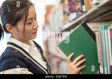 Jeune étudiante mettant un livre vert sur une étagère dans la bibliothèque Banque D'Images