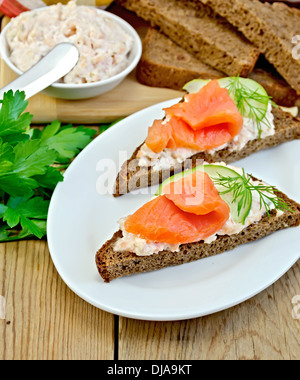 Sandwichs sur deux morceaux de pain de seigle avec de la crème, l'aneth, le concombre et le saumon dans la plaque ovale sur l'arrière-plan de planches en bois Banque D'Images