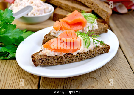 Sandwichs sur deux morceaux de pain de seigle avec de la crème, l'aneth, le concombre et le saumon dans une assiette blanche sur un fond en bois Banque D'Images