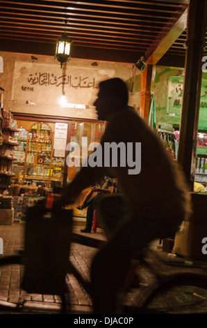 Un résident local monte un vélo à nuit à travers les rues de Deira grand souk. Dubaï, Émirats arabes unis. Banque D'Images