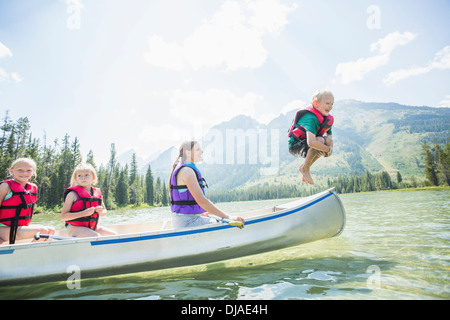 Caucasian boy jumping de canoe dans le lac Banque D'Images