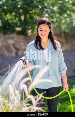 Mixed Race woman watering plants in garden Banque D'Images