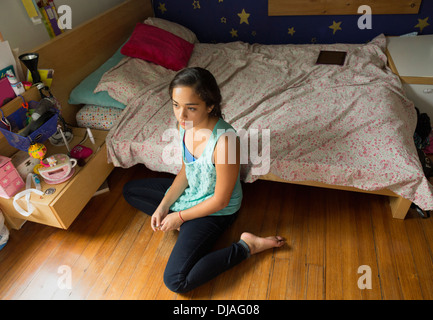 Mixed Race girl sitting on plancher de chambre à coucher Banque D'Images