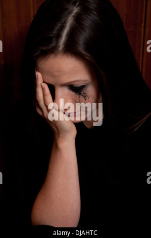 Jeune femme en colère avec son maquillage d'oeil fonctionnant en bas de son visage de larmes et sa tête dans ses mains. Banque D'Images