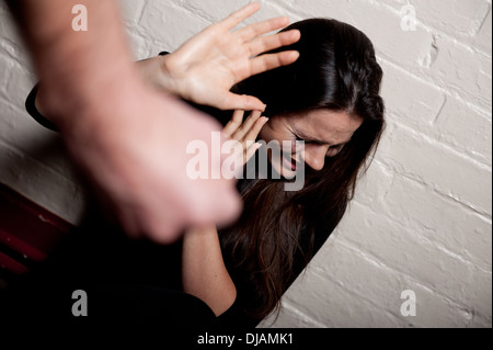 La violence domestique -Jeune femme contre un mur blanc essayant de se protéger de l'homme un poing serré. Banque D'Images