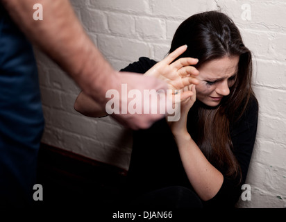 La violence domestique -Jeune femme contre un mur blanc essayant de se protéger de l'homme un poing serré. Banque D'Images