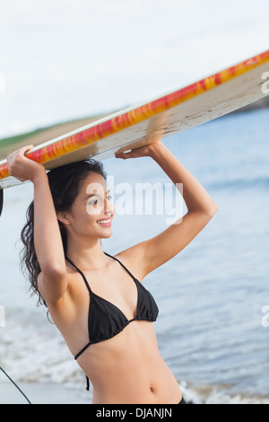 Bikini woman holding surfboard over head at beach Banque D'Images