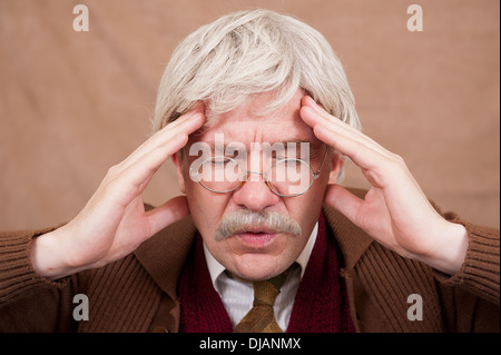 Vieil homme aux cheveux gris, les yeux fermés et les mains à la tête souffrant d'un mal de tête. Banque D'Images