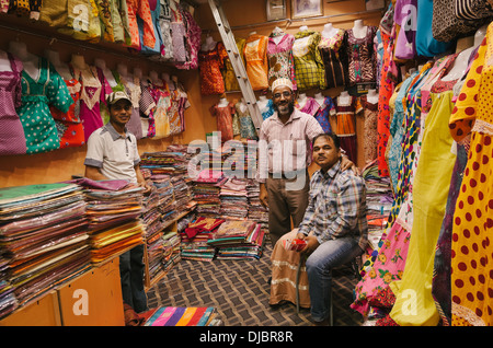 Trois hommes arabes au milieu d'un magasin de tissus colorés à Deira. Dubaï, Émirats arabes unis. Banque D'Images