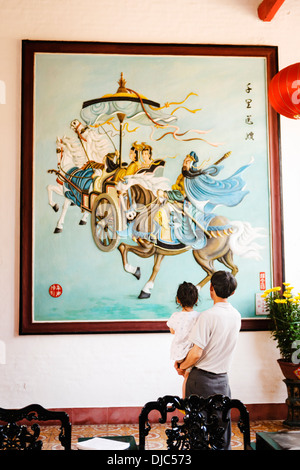 Un père et sa fille à admirer une peinture dans la salle de l'Assemblée cantonaise, Hoi An, Vietnam. Banque D'Images